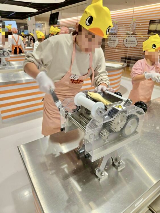 チキンラーメンファクトリーで、製麺機で伸ばしている様子。子どもでも操作できるようスタッフのサポートがあります。