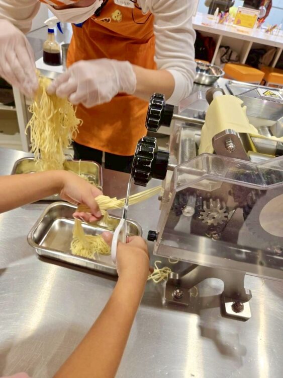 チキンラーメンファクトリーで、細く切り出された麺をハサミでカットしている子どもの様子。